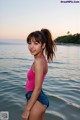 A woman in a pink tank top and denim shorts standing in the water.