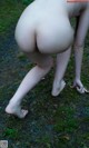 A naked woman bending over in the grass.